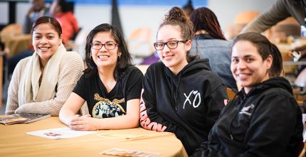group of four students sit at table and smile at camera