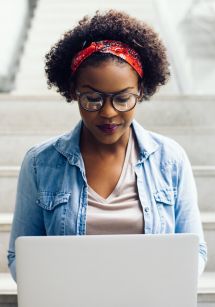 student sits on steps and looks down at laptop