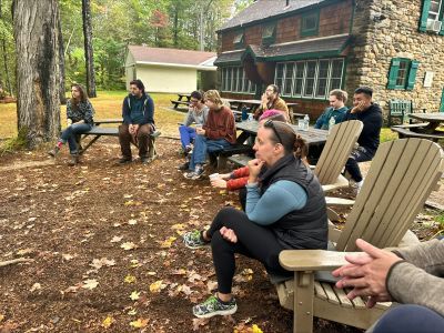 students sit outside in benches and chairs watching something that's off camera