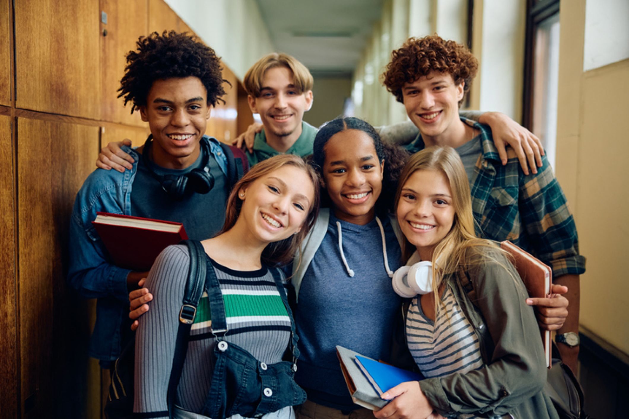 group of middle schoolers holding bags and books smile at camera