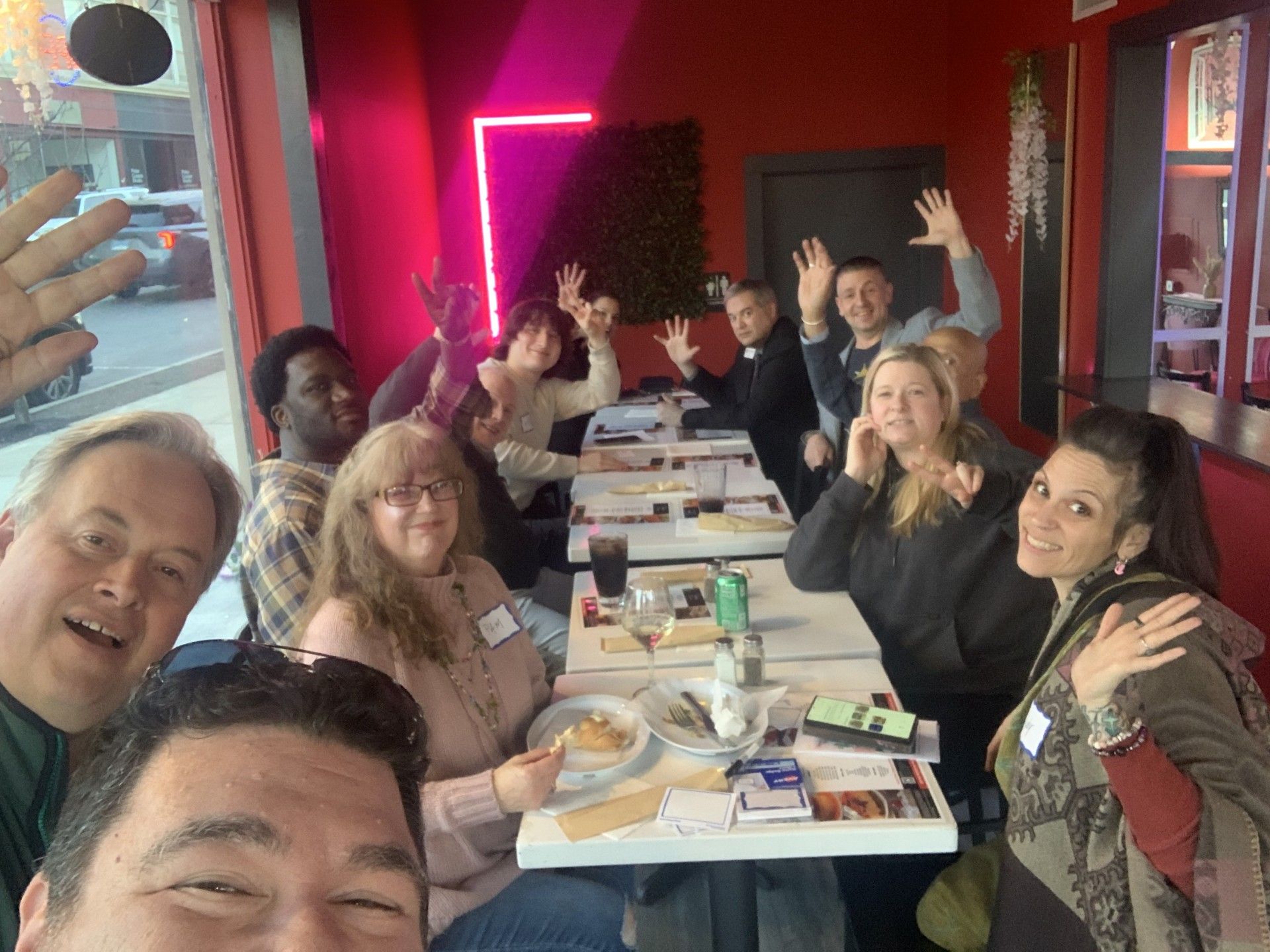 Large group smile and wave at camera from around tables in Vega Restaurant.