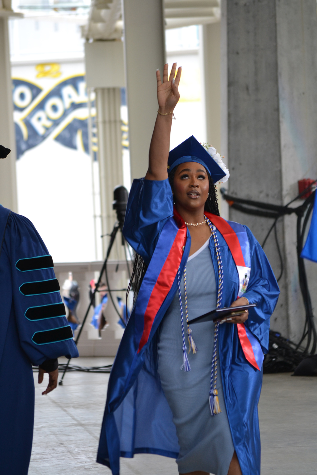 walking graduate raises her hand and looks above