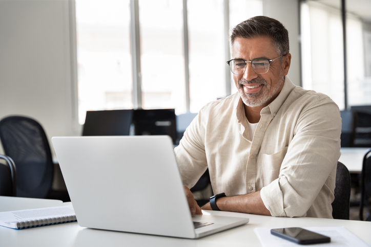 man smiles while working on laptop
