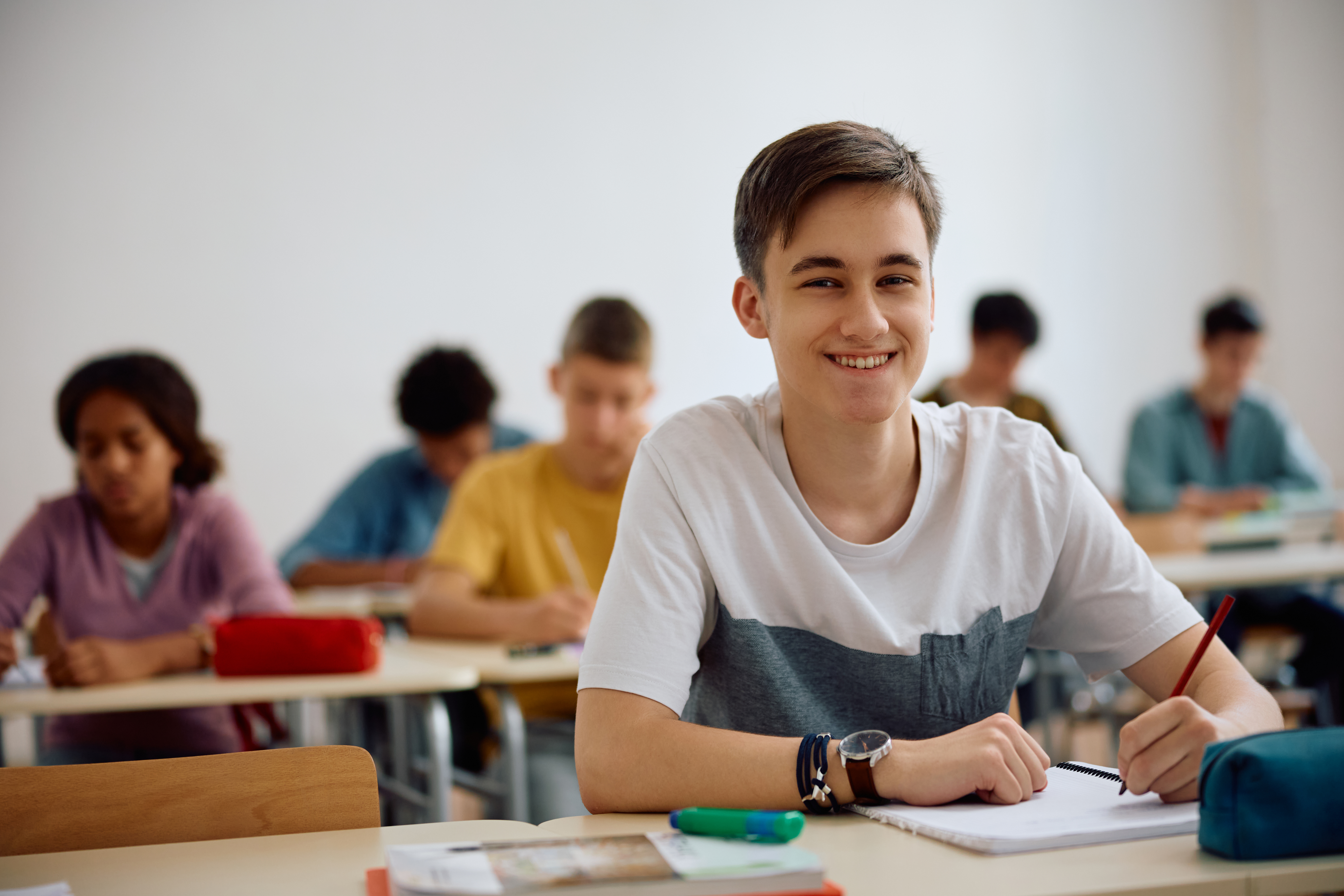 High schooler sits at desk and smiles