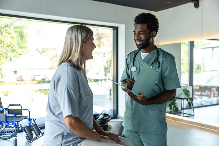 male nurse holds chart and speaks to seated patient