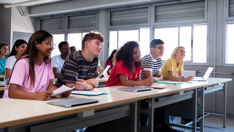 Panoramic image of multiracial happy, smiling college students in classroom listening to lecture