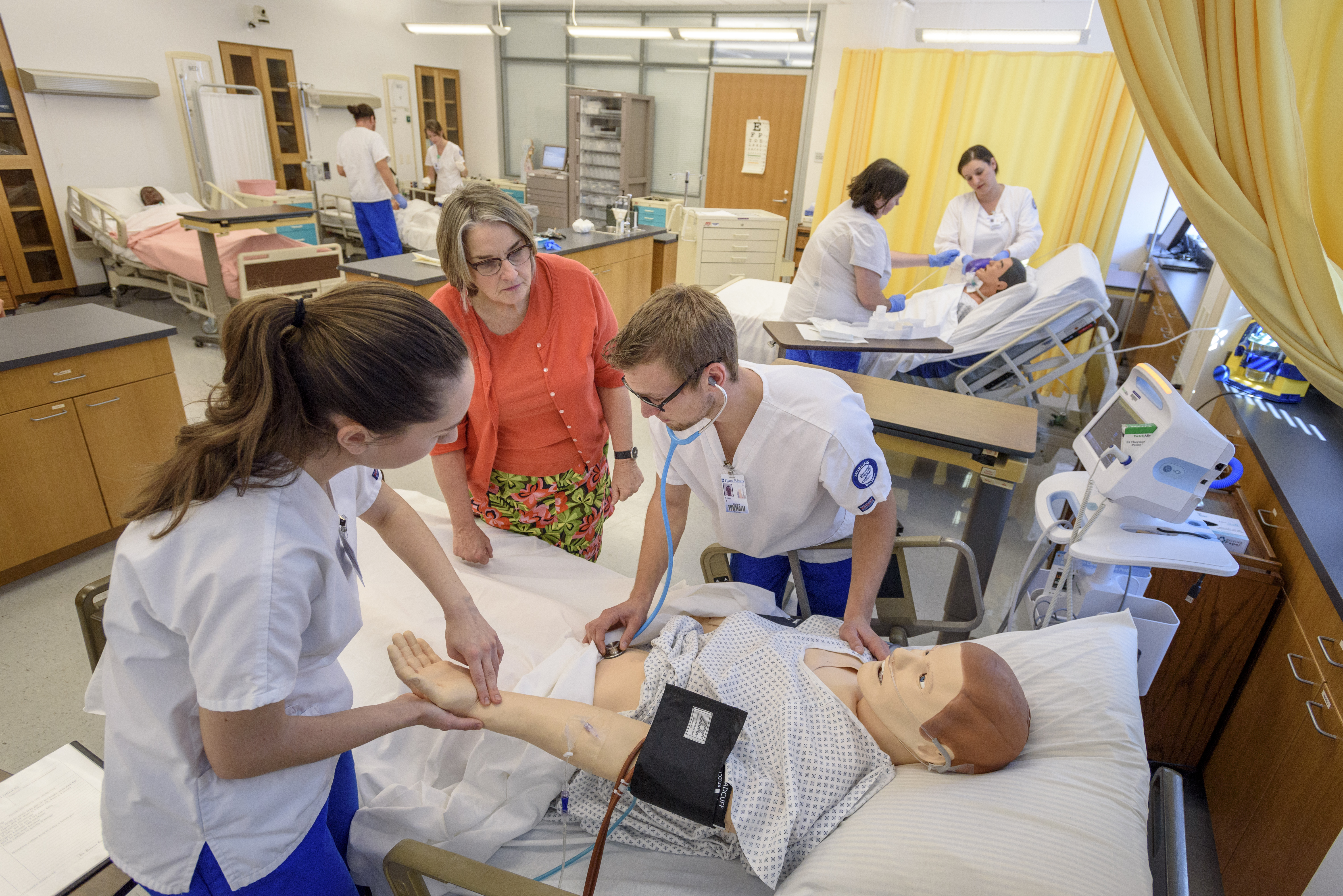Instructor helps students with dummy patient in lab setting.
