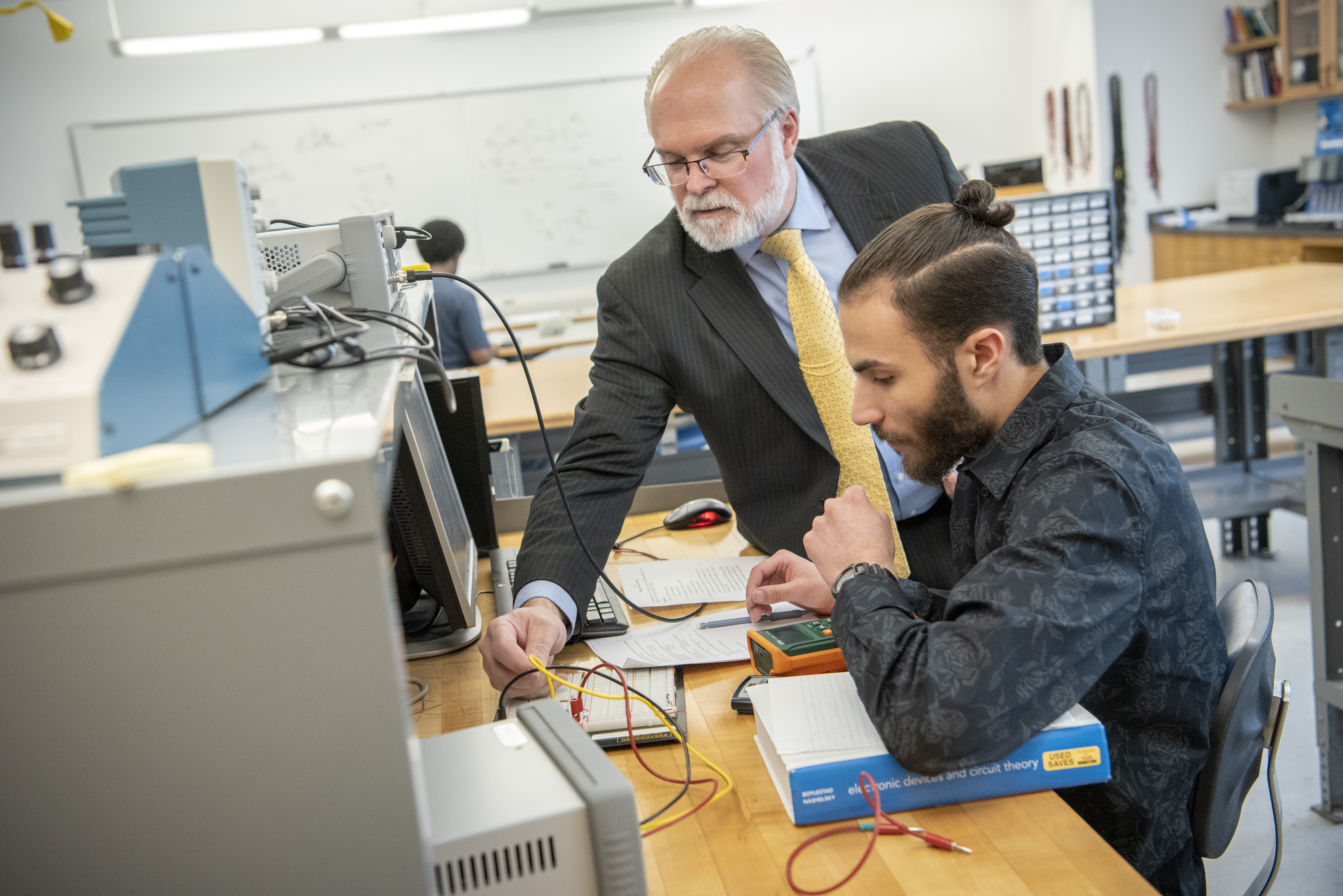 Professor helps student with wires in lab setting.