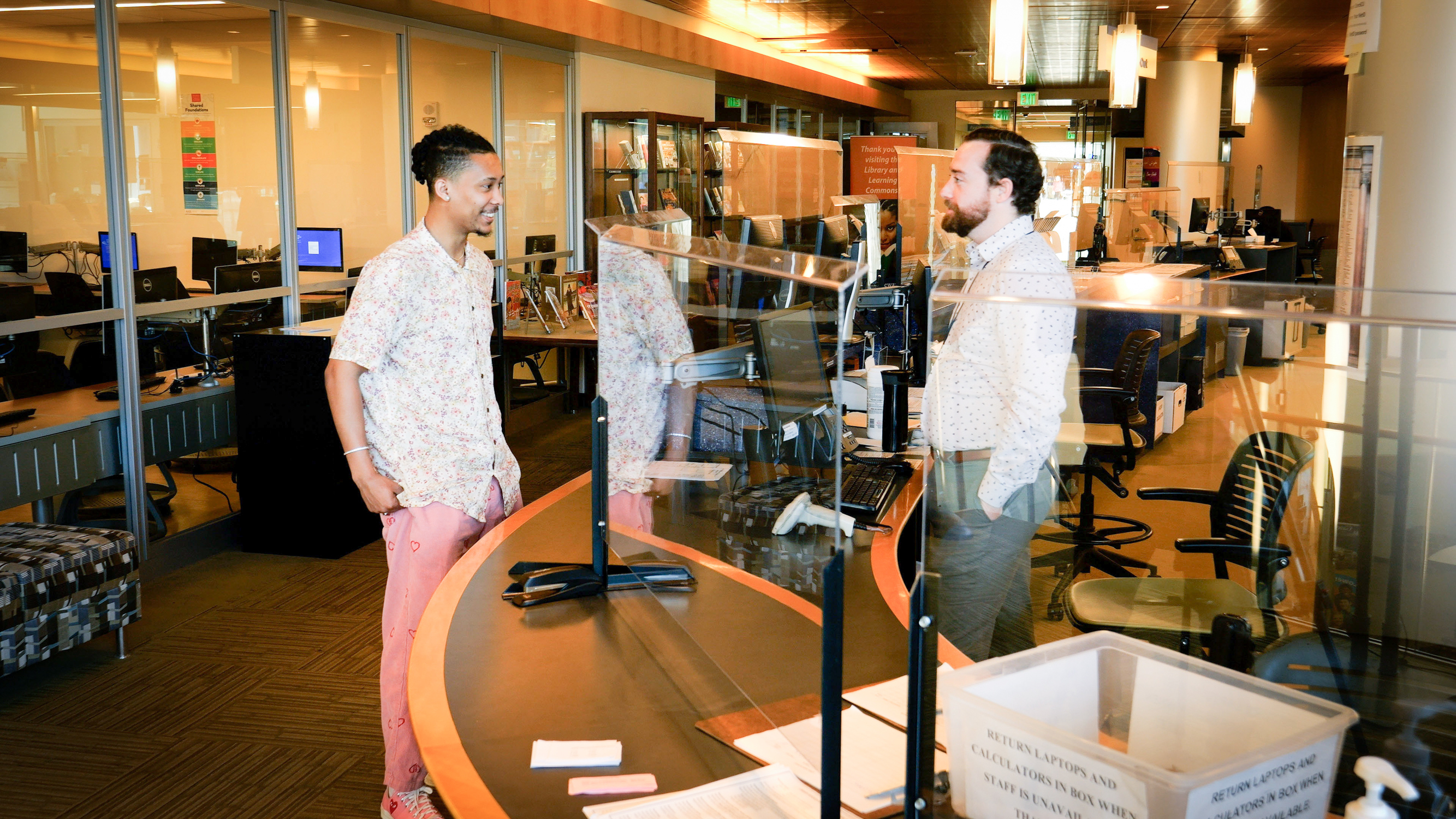 Male student and librarian talk at information desk in Gateway campus library