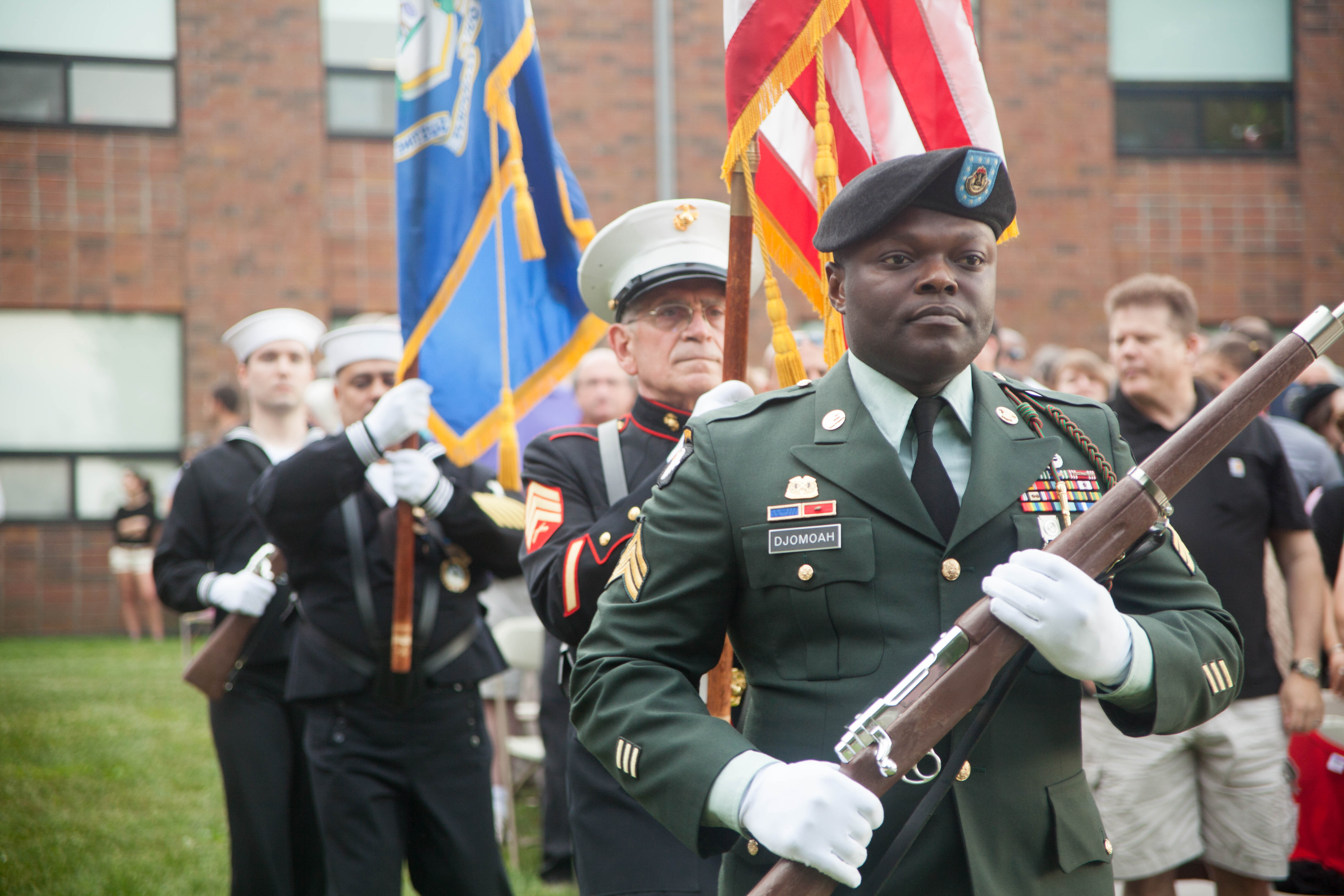 decorated military servicemen and women march holding flags at graduation ceremony