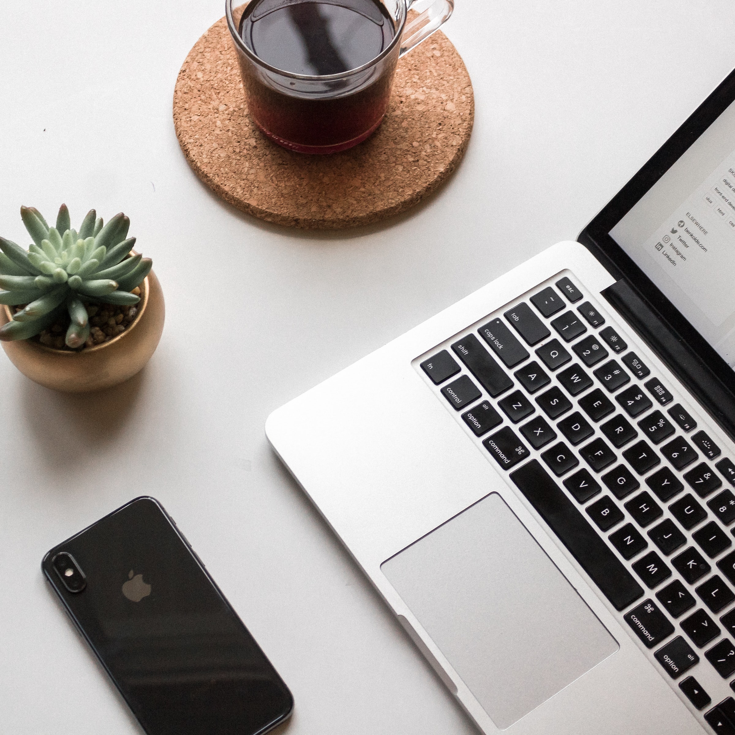 desk top showing laptop, small cactus plant, coffee mug, and cell phone