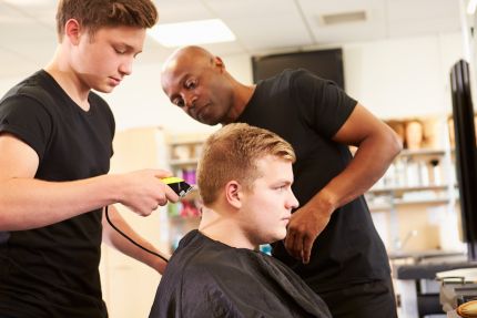 student gives client buzz cut while instructor watches