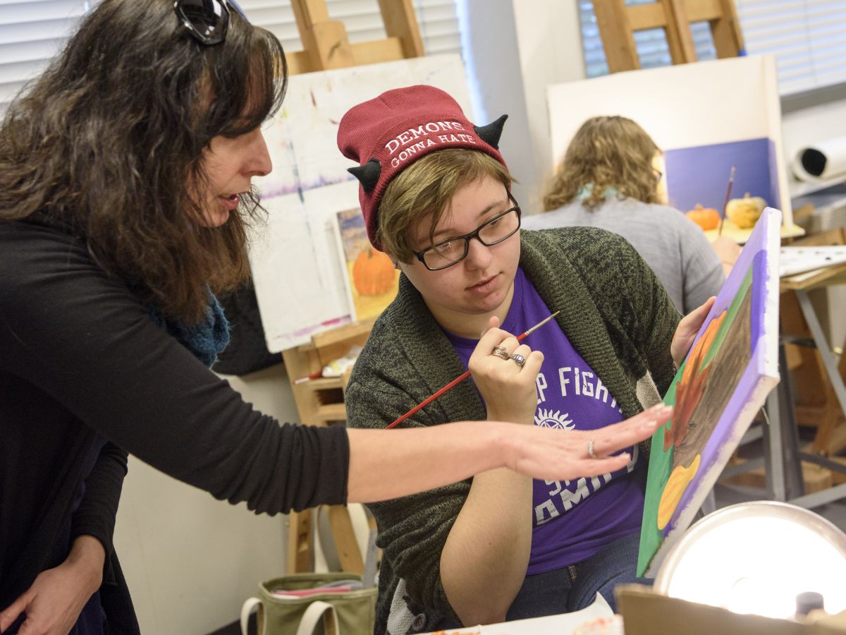 Art professor critiques student painting with student.