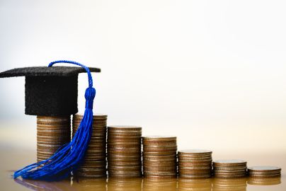row of coins stacked in descending order with small graduation cap on tallest stack