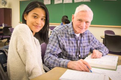 two students sit at desk together in classroom working on classwork