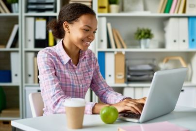 student sits at table with coffee and snack, working on laptop