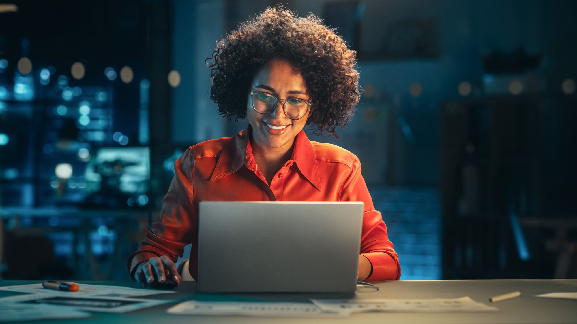 woman in dark room looks down at lit laptop screen smiling