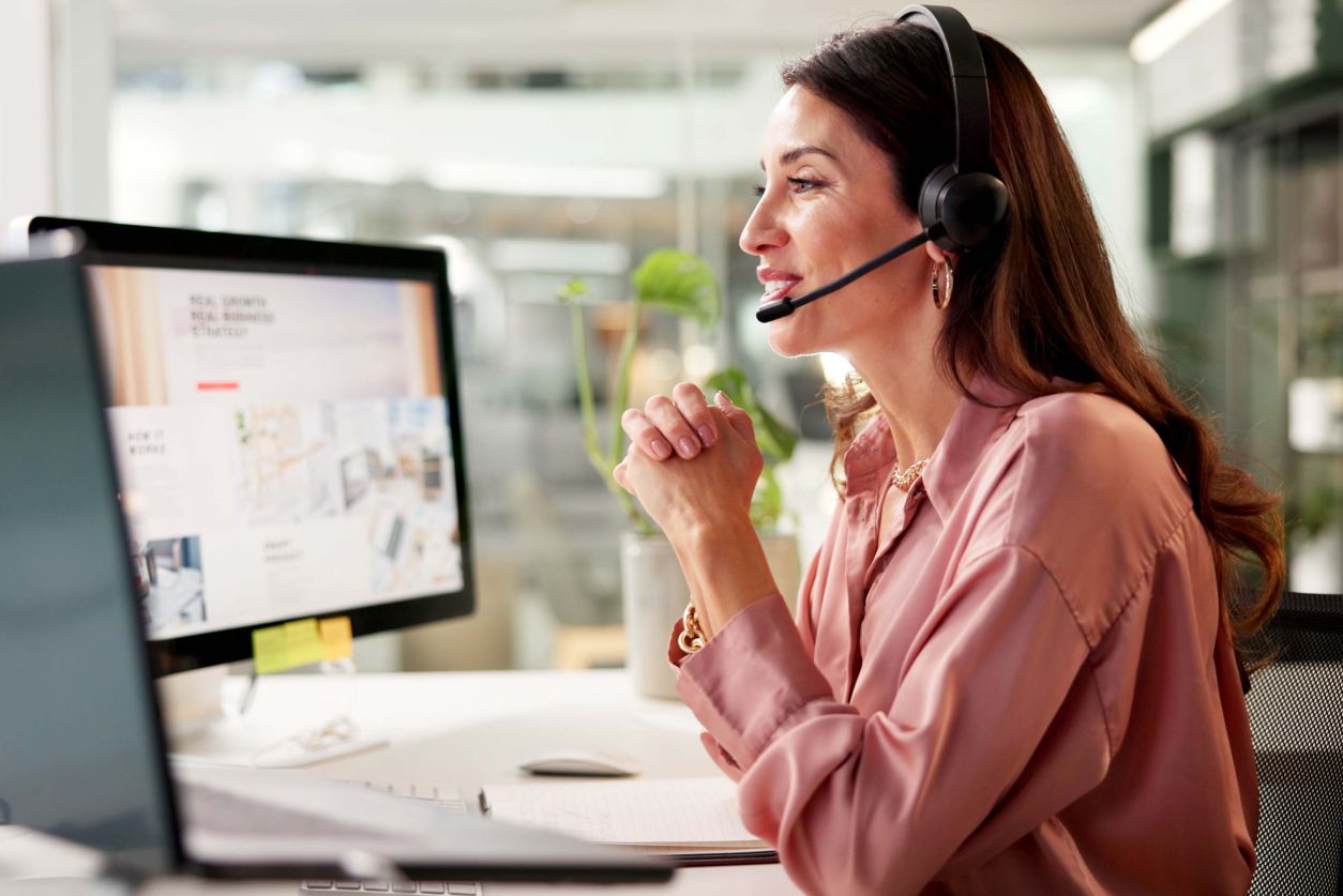 tech support person speaks on headset while looking at two computer screens in bright airy office