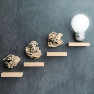 three crumbled paper bags going up steps until top step is lit lightbulb