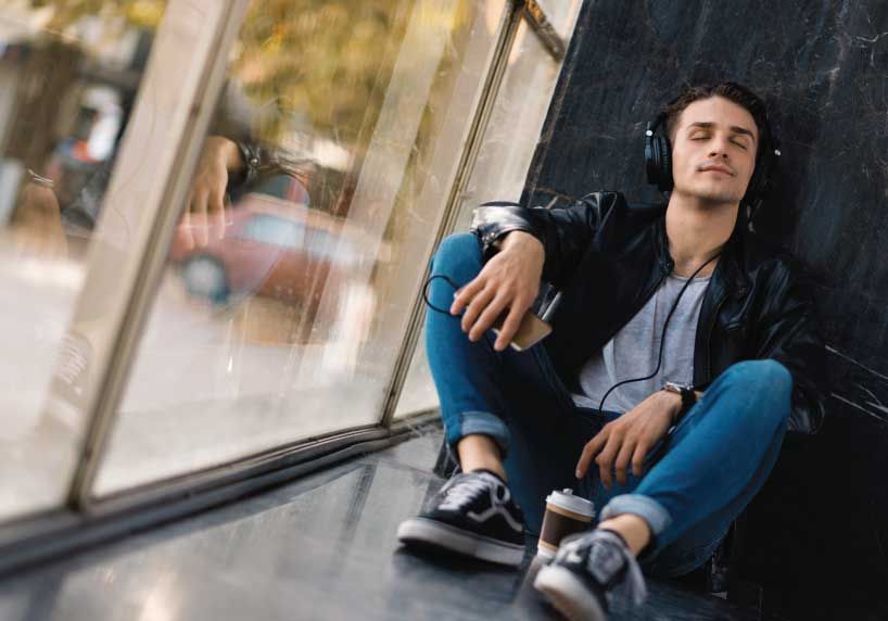 Student sits on windowsill with headphones, eyes closed enjoying music