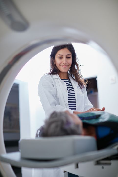 doctor holds patient's hand and smiles at them while they prepare to enter MRI machine.