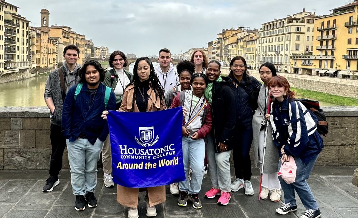 Study abroad students stand with Housatonic study abroad flag in European city.