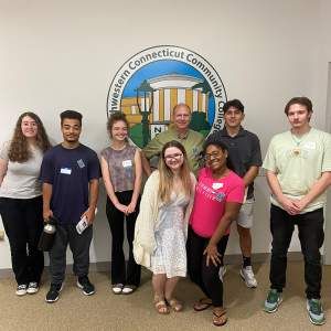 group of students smile in front of wall with NW logo on it.