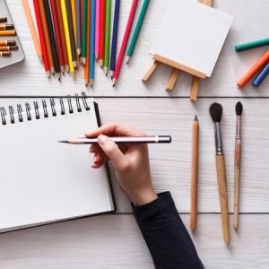 Hand drawing in journal with art supplies around.