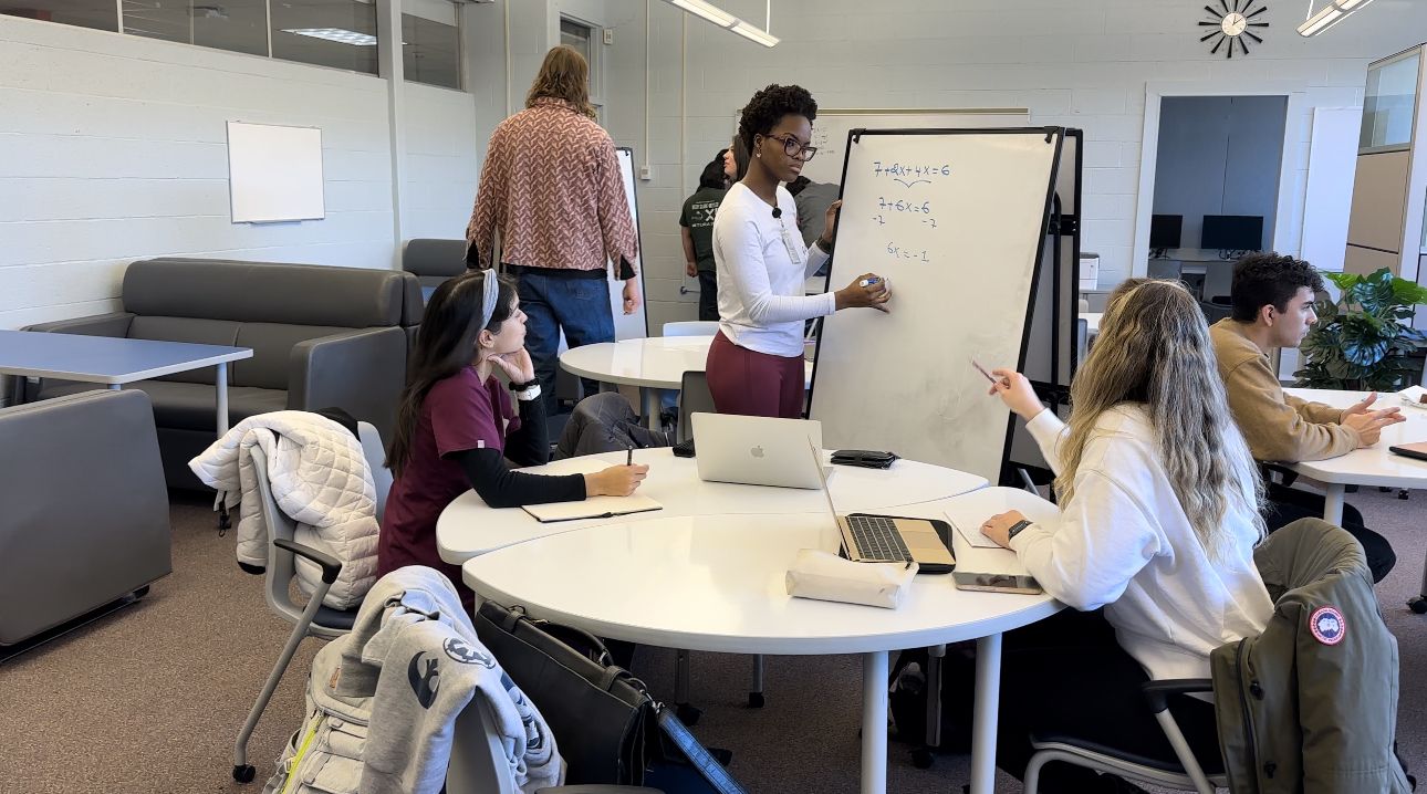 tutor writes on whiteboard while students ask questions