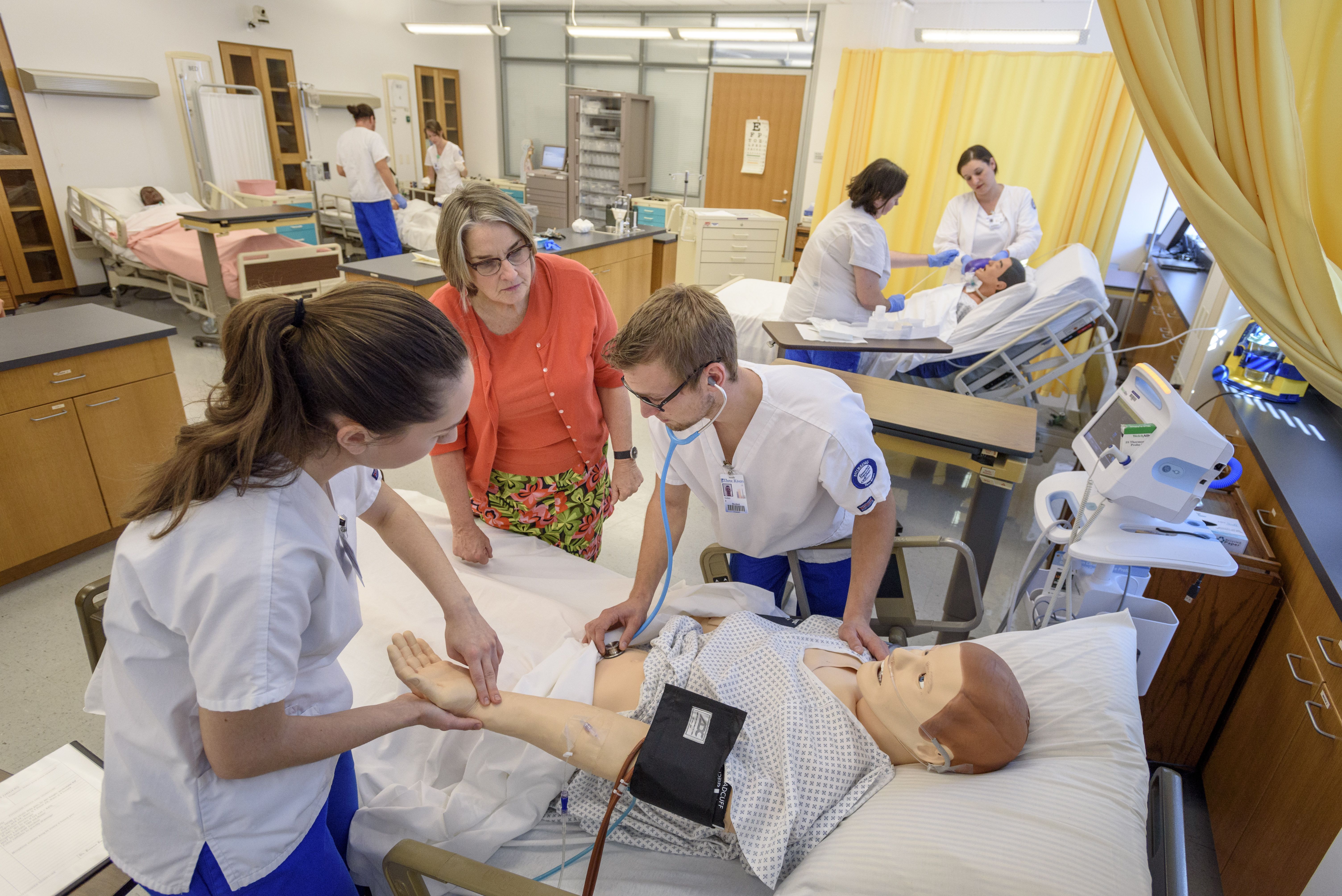 Instructor helps students with dummy patient in lab setting.