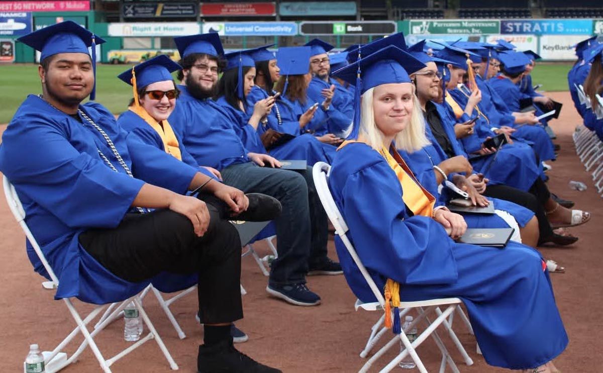 Students sit in field at commencement ceremony.