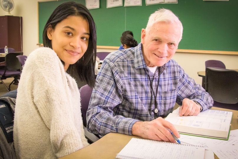 two students sit at desk together in classroom working on classwork
