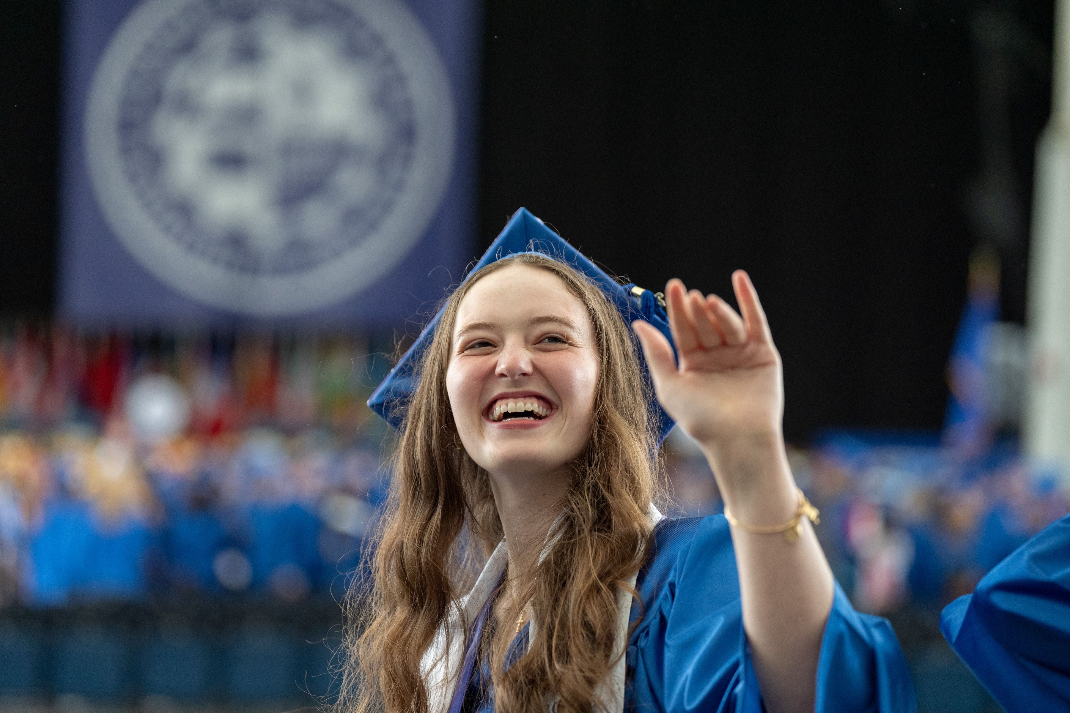 Graduate smiles and waves to someone off-camera.