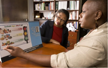 One person shows another a food chart on a table in library.