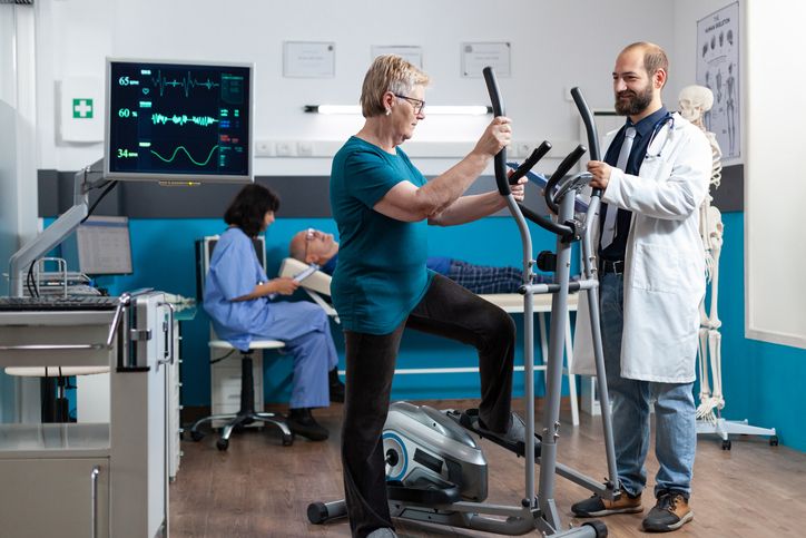 doctor helps patient climb onto elliptical machine