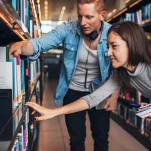 Students look at books on library shelf.