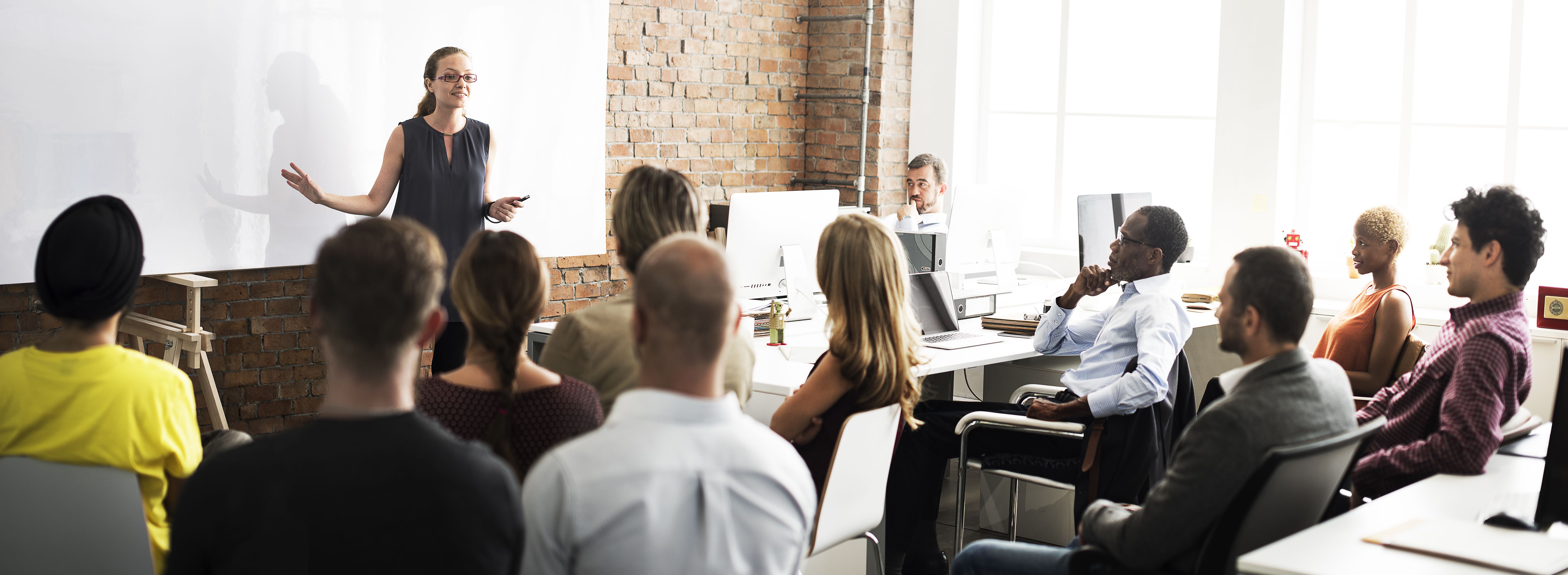 instructor speaks in front of group of business people in small, brick-walled room