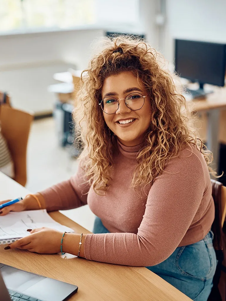 student sits at desk with papers and pen