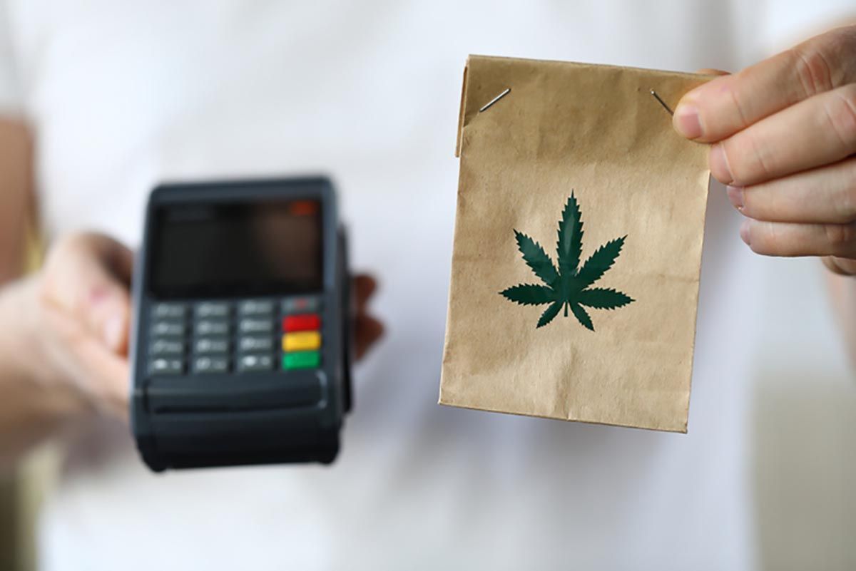 Man holding paper with cannabis leaf on it along with a credit card  payment device