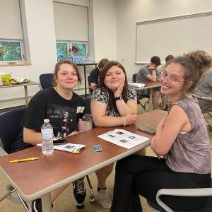 three female students sit at table and smile at camera