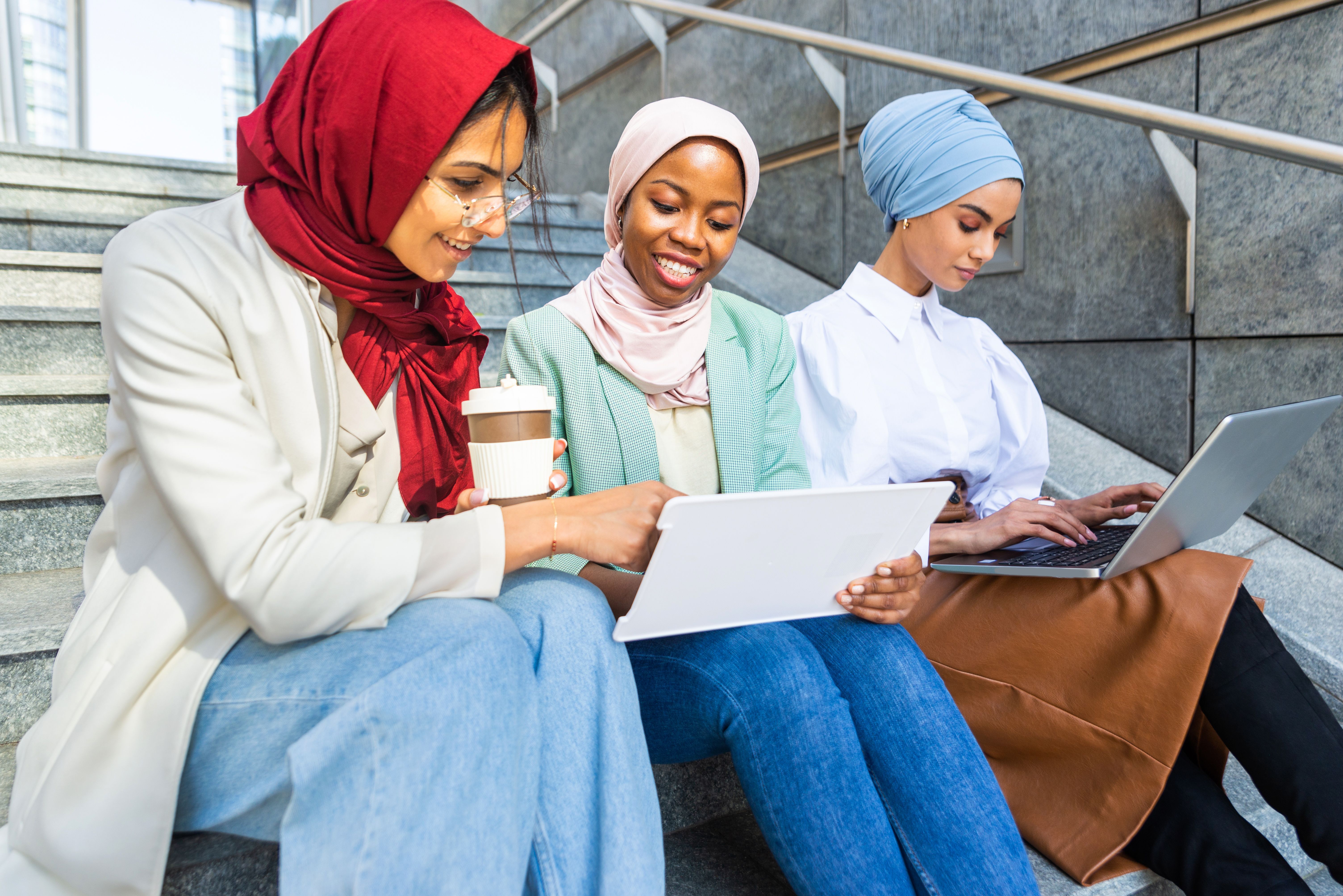 three students wearing hijabs work together on steps