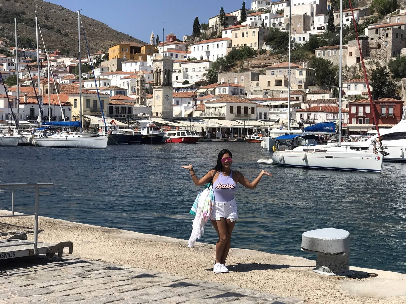 student poses in front of water and hilltop houses