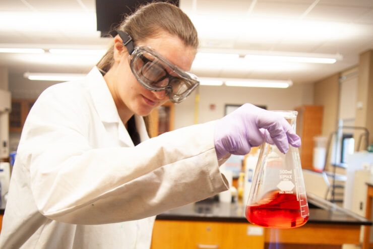 student wearing safety goggles holds beaker of red liquid in lab