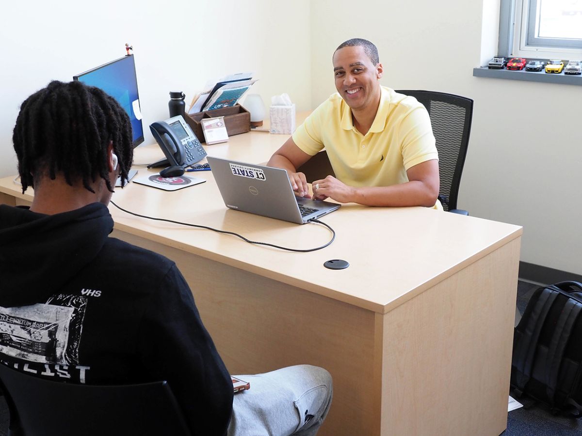 Advisor sits at desk facing student ready to help pick classes.
