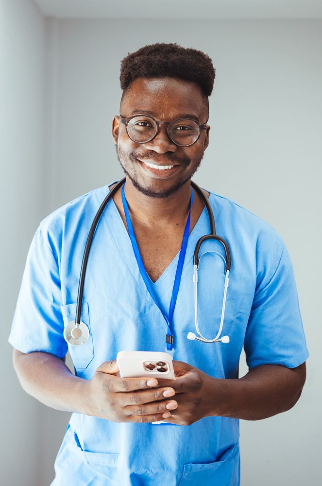 male nurse holding phone in blue scrubs with stethescope around neck smiles at camera