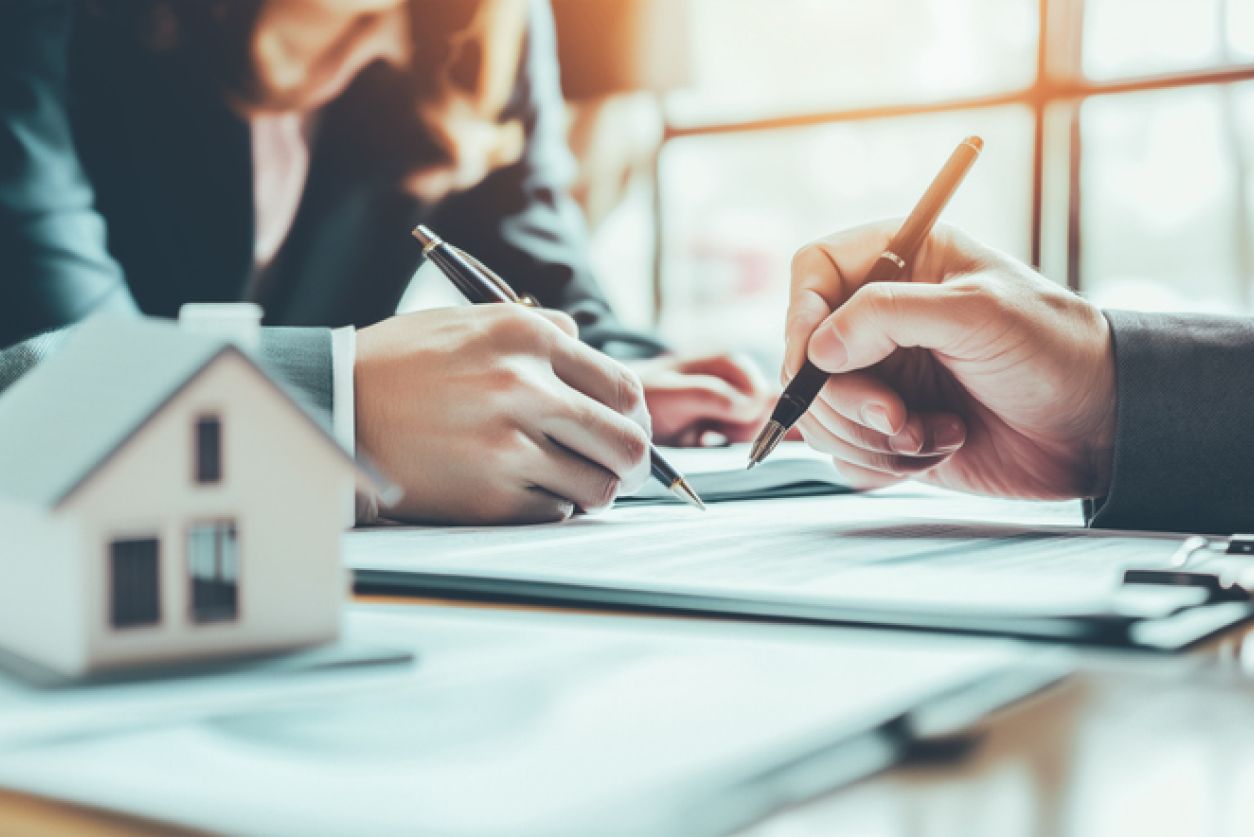 man and woman fill out paperwork with small house paperweight representing the property aspect