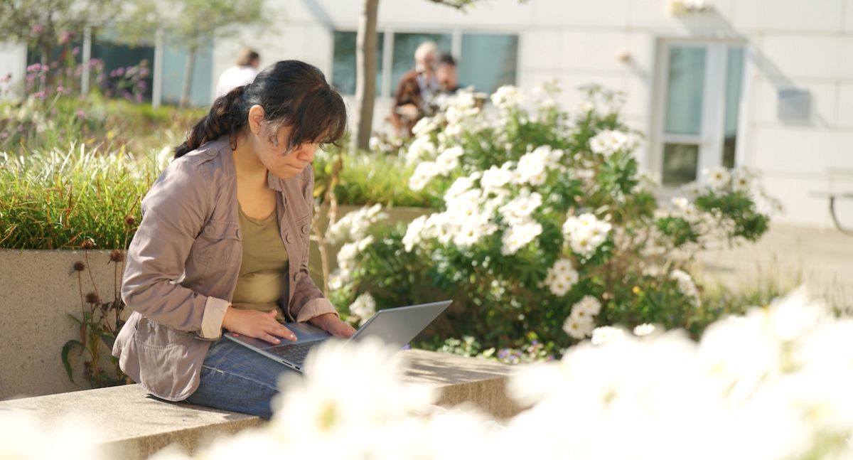 student looks down at laptop sitting on Gateway campus rooftop patio