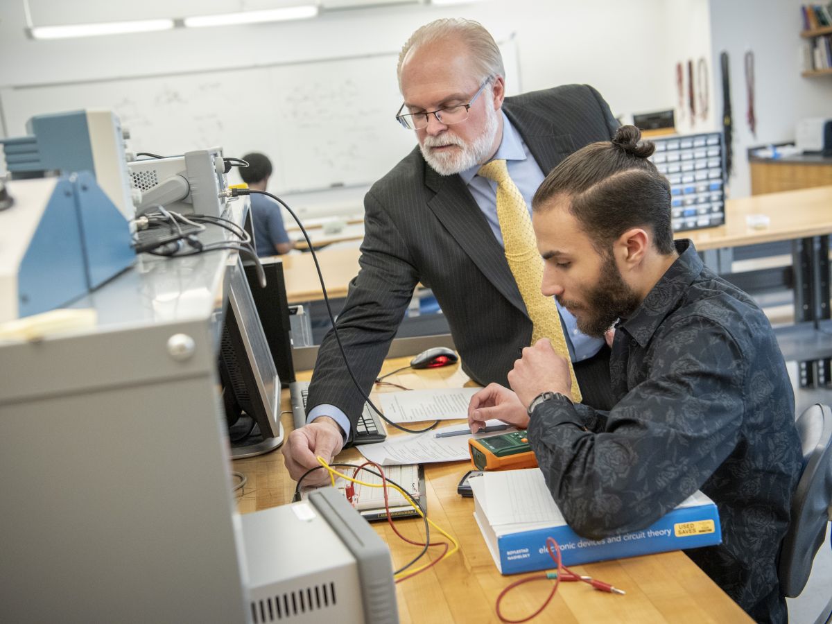 Professor helps student with wires in lab setting.