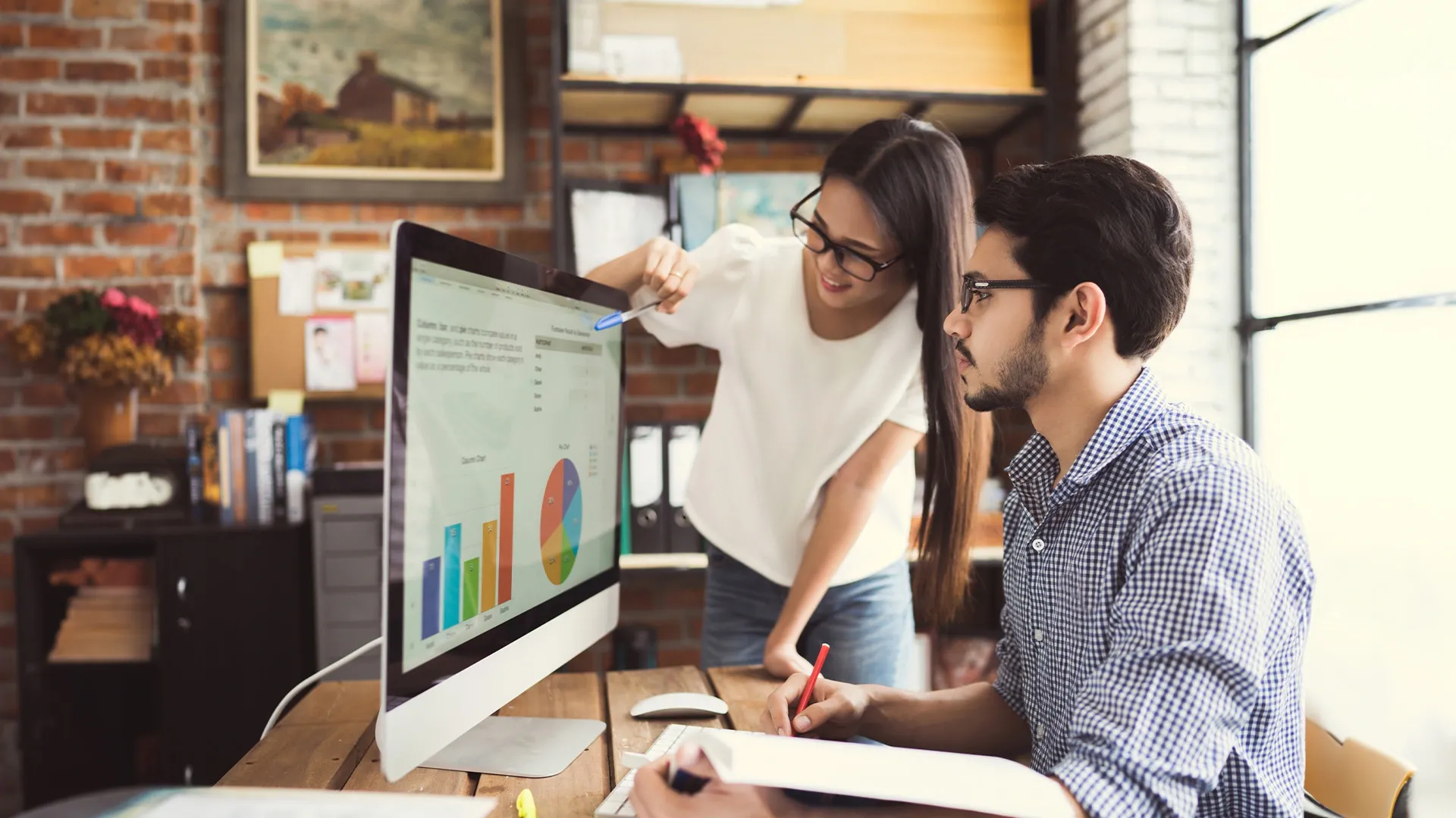 two people look at charts on large computer screen together