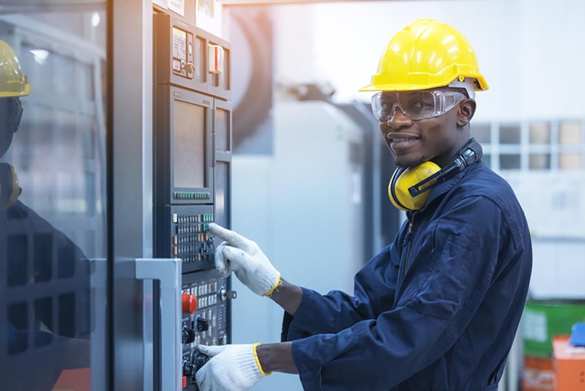 Man with yellow hard hat and safety goggles working on a machine